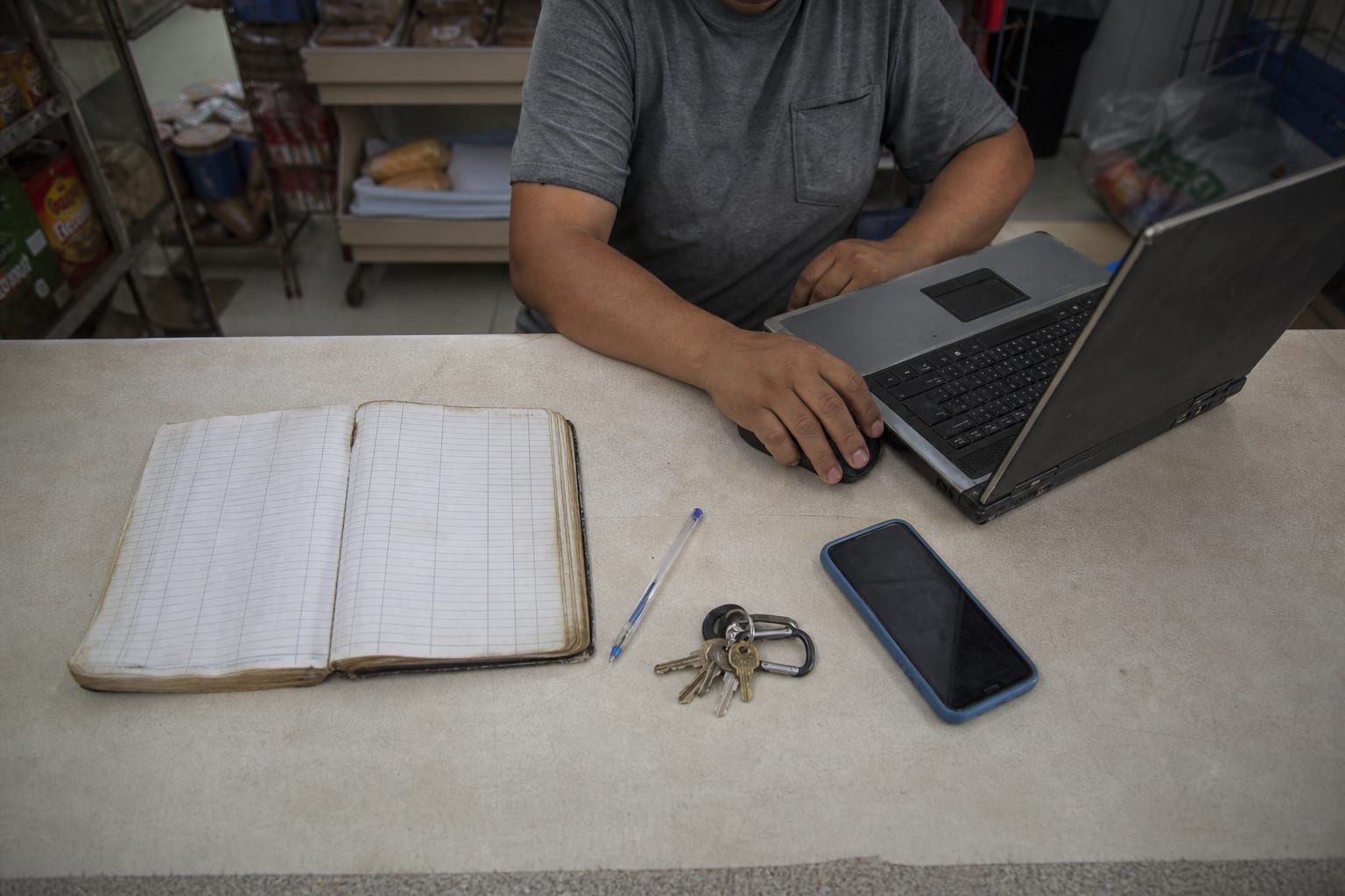 Caderno, notebook e celular lado a lado sobre o balcão de uma mercearia