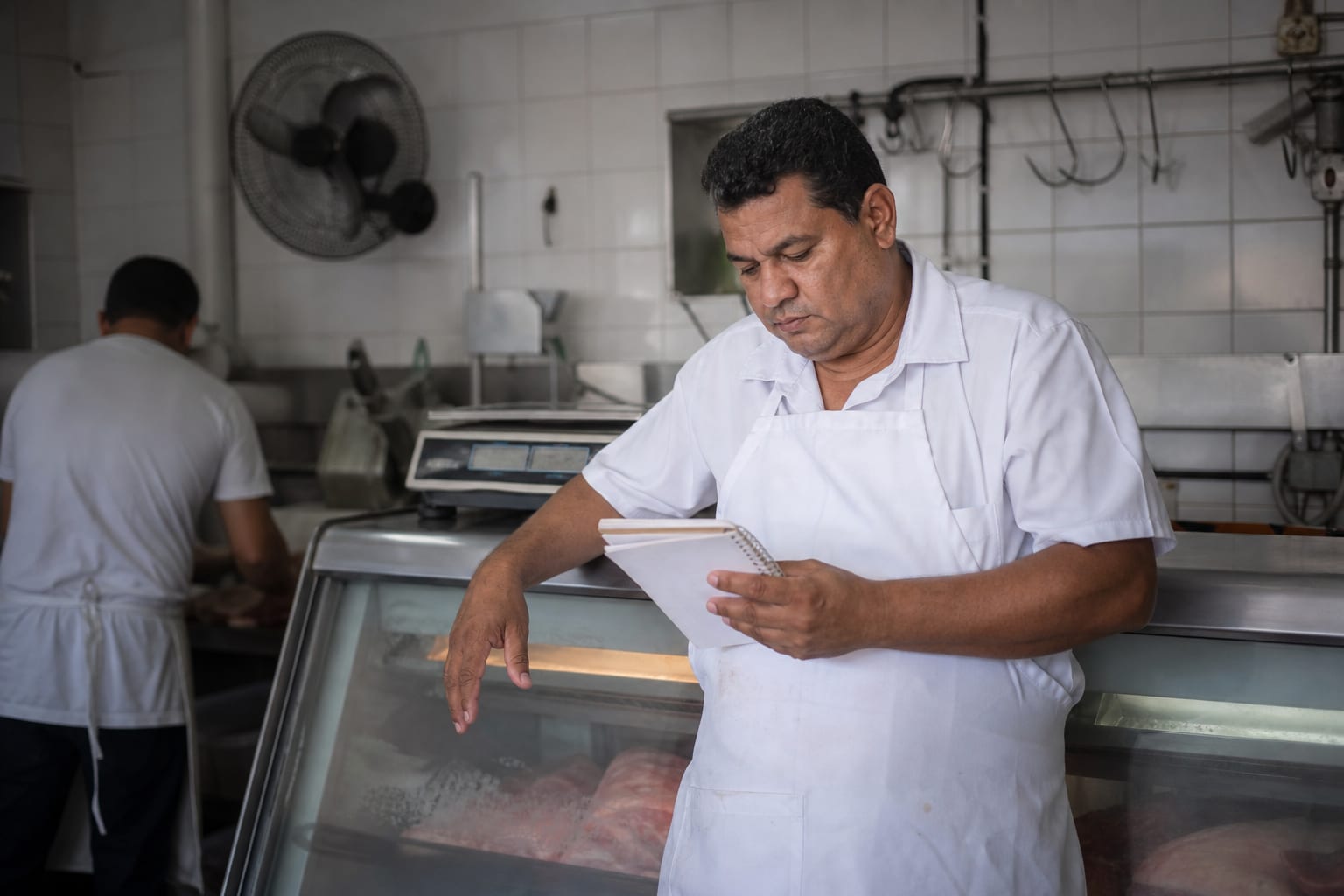 Açougueiro de avental confere anotações no balcão refrigerado no fim do expediente